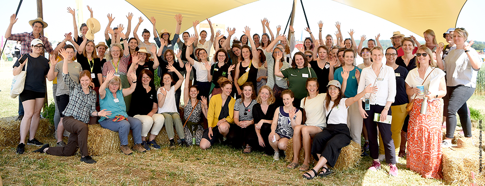Group of women gathering and waving at an outdoor agricultural event.